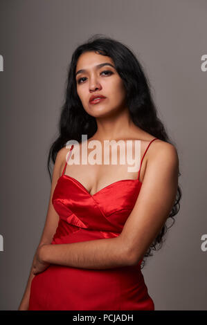 Studio Portrait Session von 17 Jahre alten Jugendlichen Mädchen mit einem roten Kleid auf einem grauen Hintergrund Stockfoto