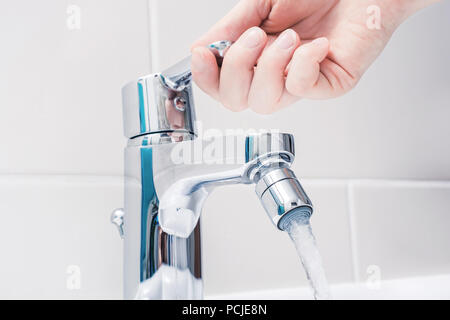 Weibliche Hand auf den Griff eines Chrom Wasserhahn mit fließendem Wasser Stockfoto