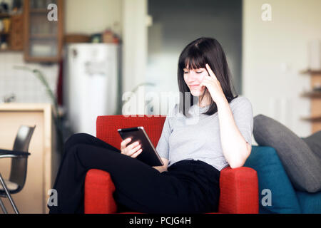 Lächelnde Frau sitzt in einem Sessel mit einem digitalen Tablet Stockfoto