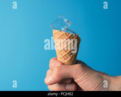 Hand ein Eis Kegel mit Eiswürfel auf blauem Hintergrund, heißen Sommer Konzept Stockfoto