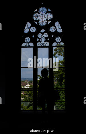 Silhouette der jungen Frau und Fenster aus dem Inneren der Kreuzgang im Basler Münster (Kirche und ehemalige Kathedrale) in Basel, Schweiz. Stockfoto