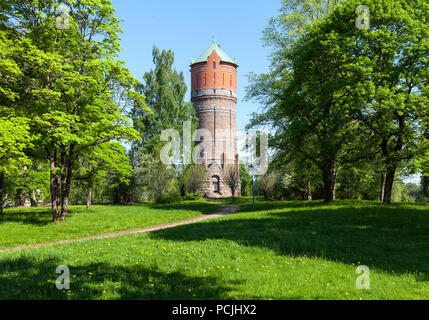 Blick auf den Wasserturm von Backsteinen. Bäume rund um, Feder und Sonnenschein. Stockfoto