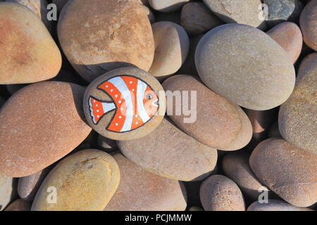 Stein mit gemalten Fisch am Kieselstrand der Jurassic Coast in Devon Stockfoto