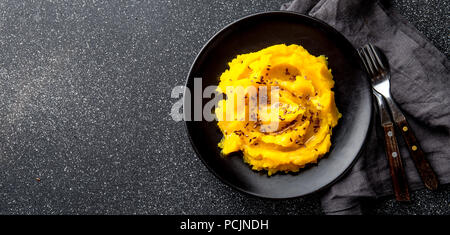 Kartoffelpüree mit Kürbis in schwarz Schüssel. Der dunkle Hintergrund. top View Stockfoto