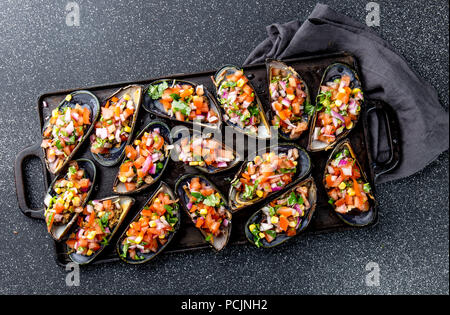 Peruanisches Essen. Choros a la chalaca. Große Muscheln, Choros zapatos gewürzt mit lila Zwiebeln, Tomaten, Mais und Zitrone. Ansicht von oben, schwarzen Hintergrund. Die peruanische Gericht Stockfoto