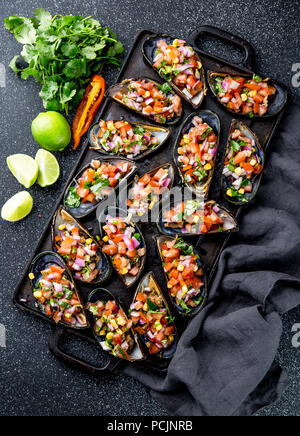 Peruanisches Essen. Choros a la chalaca. Große Muscheln, Choros zapatos gewürzt mit lila Zwiebeln, Tomaten, Mais und Zitrone. Ansicht von oben, schwarzen Hintergrund. Die peruanische Gericht Stockfoto