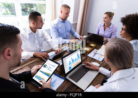 Gruppe der Geschäftsleute, die Analyse von Graphen mit elektronischen Gadgets Stockfoto