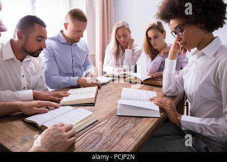 Gruppe von Jungen multiethnischen Menschen Lesen der Bibel über Holz- Schreibtisch Stockfoto