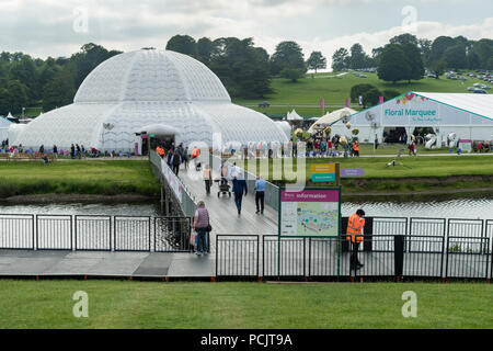 Leute an der RHS Chatsworth Flower Show Wandern & Kreuzung temporäre River Bridge, die zu großen festzelten an belebten Showground - Derbyshire, England, UK. Stockfoto