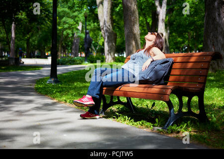 Rothaarige Frau, Sonnenbaden im Park und auf der Bank sitzen Stockfoto