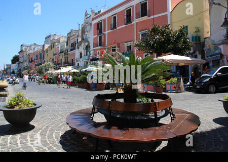 Viele Touristen entlang der Promenade auf Procida, Italien bummeln, mit bunten Häusern in verschiedenen Pastelltönen im Hintergrund gemalt Stockfoto