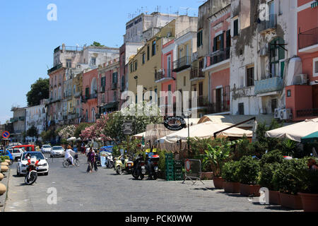 Viele Touristen entlang der Promenade auf Procida, Italien bummeln, mit bunten Häusern in verschiedenen Pastelltönen im Hintergrund gemalt Stockfoto