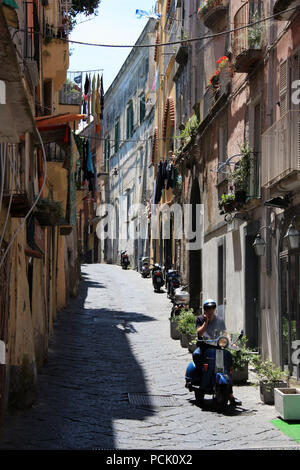 Ein Mann auf dem Mobiltelefon während der Fahrt seine Vespa durch einen typischen schmalen Gasse auf Procida, Golfo di Napoli, Italien Moped Stockfoto