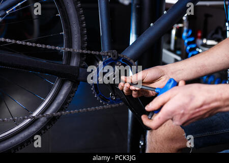 Eine Nahaufnahme der Hand eines männlichen Fahrradmechaniker in der Werkstatt verwendet einen Schraubendreher Werkzeug an das Fahrrad Handkurbel, Reparieren und Einstellen der vorderen Rad s Stockfoto