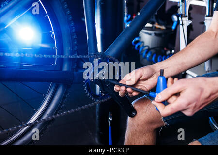 Eine Nahaufnahme der Hand eines männlichen Fahrradmechaniker in der Werkstatt verwendet einen Schraubendreher Werkzeug an das Fahrrad Handkurbel, Reparieren und Einstellen der vorderen Rad s Stockfoto