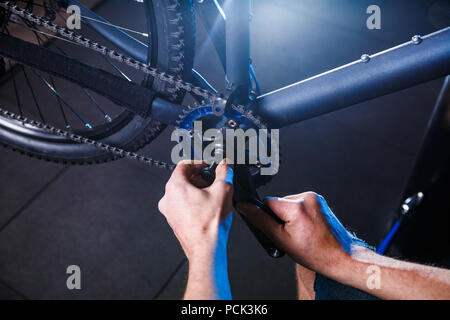 Eine Nahaufnahme der Hand eines männlichen Fahrradmechaniker in der Werkstatt verwendet einen Schraubendreher Werkzeug an das Fahrrad Handkurbel, Reparieren und Einstellen der vorderen Rad s Stockfoto