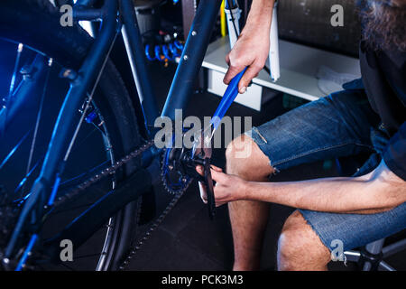 Eine Nahaufnahme der Hand eines männlichen Fahrradmechaniker in der Werkstatt verwendet einen Schraubendreher Werkzeug an das Fahrrad Handkurbel, Reparieren und Einstellen der vorderen Rad s Stockfoto