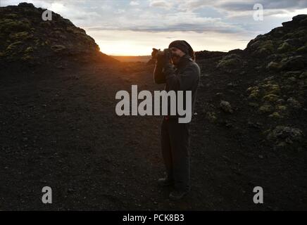 Eine abenteuerliche Fotograf klettert Krafla Vulkan und Fotos von lava Ruinen im Sonnenuntergang Stockfoto