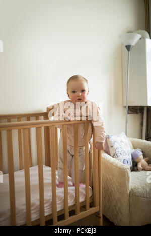 Babymädchen stehen in Krippe Stockfoto
