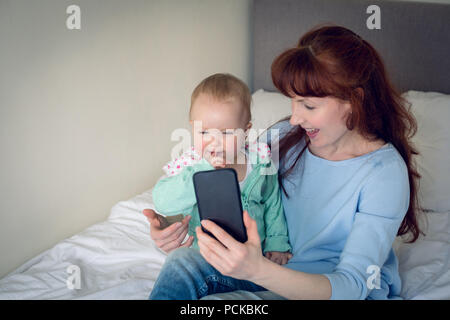 Mutter und Baby Mädchen unter selfie mit Handy im Schlafzimmer Stockfoto