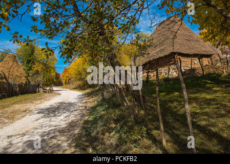 Unbefestigte Straße durch Bergdorf. Bunte Herbst Wald und Holz- Haus Stockfoto