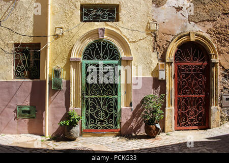 Yellów und rose Farbe der Fassade eines alten Hauses mit 2 Toren mit und Bögen und grünen und roten Gittern. Stadt in der ehemaligen portugiesischen Festung in Stockfoto