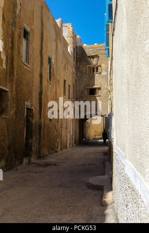 Schmale Straße mit alten Häusern, teilweise aufgegeben. Unterführung mit einem silhoutte einer Person. Strahlend blauen Himmel. Stadt in der ehemaligen portugiesischen Festung, El J Stockfoto