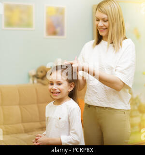 Mutter ist das Flechten der Haare stehen ihre junge Tochter im Zimmer der Kinder. Stockfoto