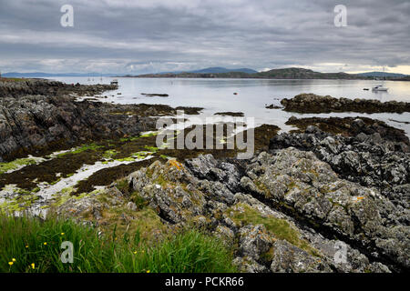 Sandstrand und felsigen Ufer unter Wolken auf der Isle of Iona mit Booten auf den Klang von Iona und Fionnphort Mull berge Schottland Großbritannien Stockfoto