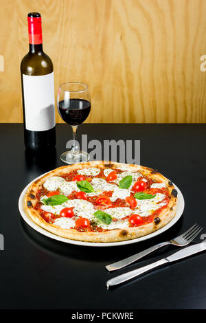 Leckere Pizza serviert mit einer Flasche und Glas Rotwein in einem Restaurant Stockfoto