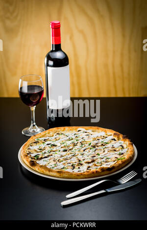 Leckere Pizza serviert mit einer Flasche und Glas Rotwein in einem Restaurant Stockfoto