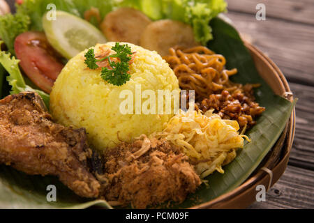 Nasi Kuning. indonesische gelber Reis mit gebratenen Hähnchen auf Bananenblatt serviert. Stockfoto