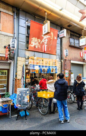 : Kuromon Ichiba, Küche essen Osaka's Markt. Die Menschen in der Warteschlange außerhalb Restaurant verkauf Soba-nudeln Buchweizen Nudeln und andere lokale Gerichte. Stockfoto