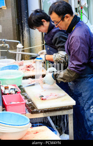 : Kuromon Ichiba, Küche essen Osaka's Markt. Zwei Männer, während Fisch, Schneiden, Arbeiten am Tisch mit laufendem Wasser aus fließenden zum Ende. Stockfoto