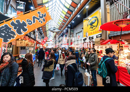 : Kuromon Ichiba, Küche essen Osaka's Markt. Blick entlang Arcade mit verschiedenen Ständen und Geschäften auf beiden Seiten der Arcade. Besetzt mit Menschen überfüllt. Winte Stockfoto