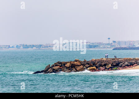 Wellen, Steinen an der Küste mit Häusern im Hintergrund, deutschen Kolonialstadt Swakopmund, Namibia Stockfoto