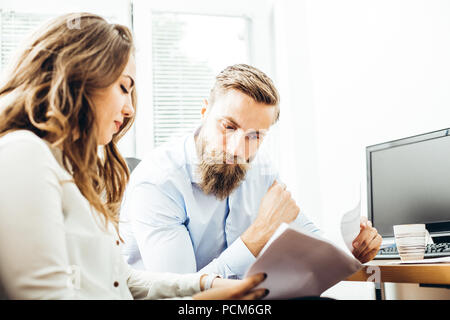 Erfolgreiche Teamarbeit: Mann und Frau am Schreibtisch sitzen, reden über Berichte und Finanzen. Dokument analysieren, Pläne. Stockfoto