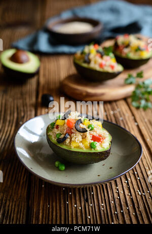 Avocado gefüllt mit Quinoa, grüne Erbsen, Tomaten, Oliven, Rote und gelbe Paprika und Petersilie Stockfoto