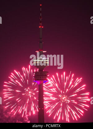 Dpatop - 02. August 2018, Deutschland, München: Der Himmel hinter dem Olympic Tower ist hell durch Feuerwerk in einem rosa Farbton beleuchtet. Das Feuerwerk war leuchtet während der Impark Sommerfest bei den Olympischen Park. Foto: Lino Mirgeler/dpa Stockfoto