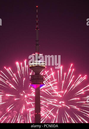 02. August 2018, München: Der Himmel hinter dem Olympic Tower ist hell erleuchtet von Feuerwerk in einem rosa Farbton. Das Feuerwerk war leuchtet während der Impark Sommerfest bei den Olympischen Park. Foto: Lino Mirgeler/dpa Stockfoto