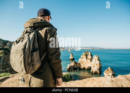 Ein Tourist oder Reisende mit einem Rucksack bewundert die schöne Aussicht auf den Atlantischen Ozean und die Küste in der Nähe der Stadt Lagos in Portugal genannt. Stockfoto