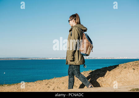 Ein Mädchen Touristen oder Reisende mit einem Rucksack Spaziergänge entlang der felsigen Küste und bewundert den schönen Blick auf den Atlantik in Portugal Stockfoto