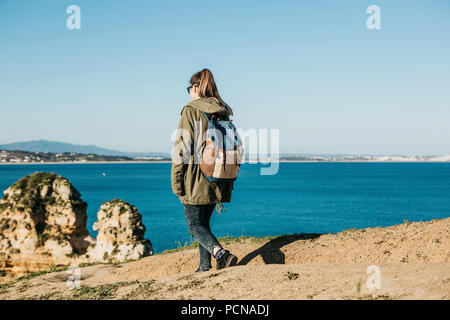 Ein Mädchen Touristen oder Reisende mit einem Rucksack Spaziergänge entlang der felsigen Küste und bewundert den schönen Blick auf den Atlantik in Portugal Stockfoto