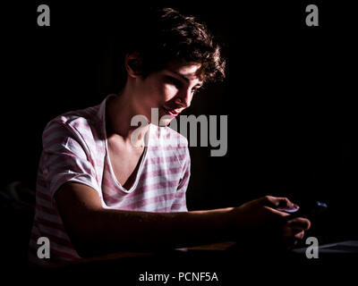 Junger Teenager scrollen Mobile Smartphone im dunklen Schlafzimmer spät in der Nacht Stockfoto