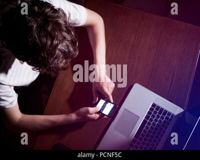 Junger Teenager scrollen Mobile Smartphone im dunklen Schlafzimmer spät in der Nacht Stockfoto