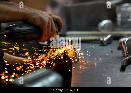 Man Hände Behandeln von Metallen Teile der Hardware in einem Workshop mit Winkelschleifer. Männliche Metallarbeiter, Polieren und Abschluss Stück der mittelalterlichen Rüstung. Stockfoto