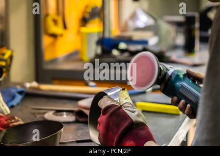 Man Hände Behandeln von Metallen Teile der Hardware in einem Workshop mit Winkelschleifer. Männliche Metallarbeiter, Polieren und Abschluss Stück der mittelalterlichen Rüstung. Stockfoto