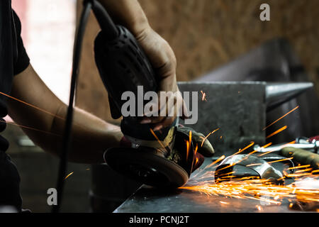 Man Hände Behandeln von Metallen Teile der Hardware in einem Workshop mit Winkelschleifer. Männliche Metallarbeiter, Polieren und Abschluss Stück der mittelalterlichen Rüstung. Stockfoto