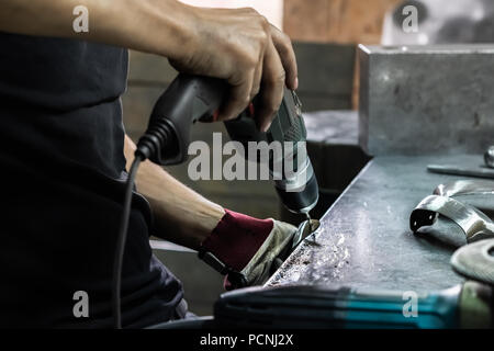 Männliche Metallarbeiter, Bohrung, ein Stück der mittelalterlichen Rüstung. Man Hände Behandeln von Metallen Teile der Hardware in einem Workshop mit elektrischen Bohrmaschine Stockfoto