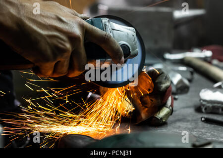 Männliche Metallarbeiter, Polieren und Abschluss Stück der mittelalterlichen Rüstung. Man Hände Behandeln von Metallen Teile der Hardware in einem Workshop mit Winkelschleifer. Stockfoto